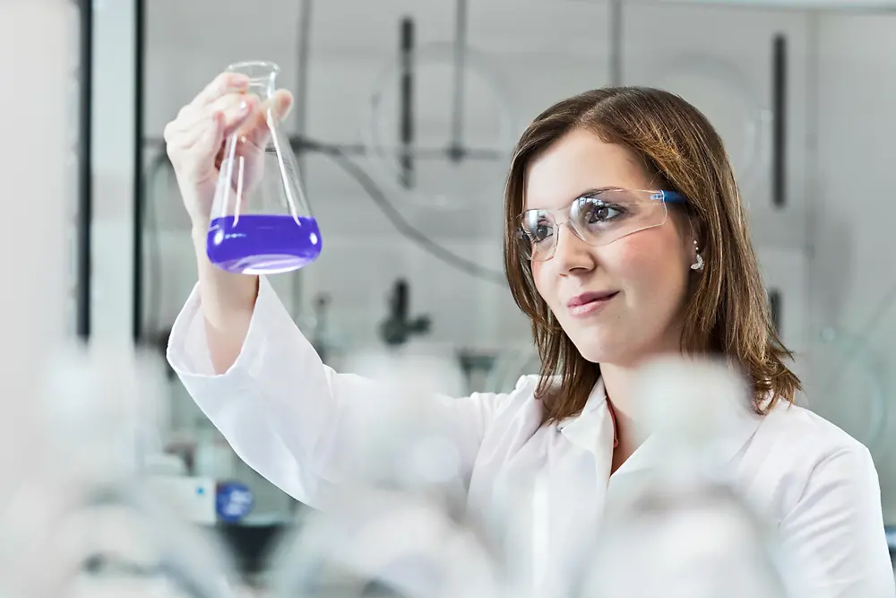 A female scientist is experimenting in a lab, wearing a lab coat and safety goggles.