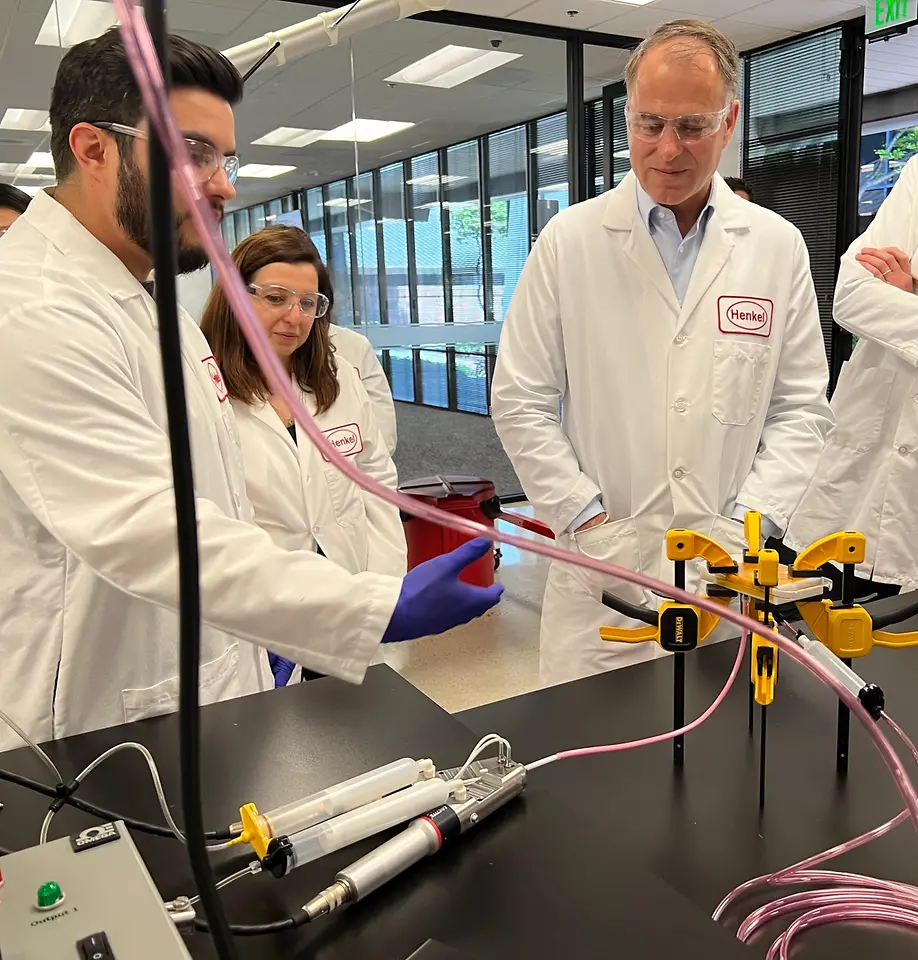 Jan-Dirk Auris (pictured right), Henkel Executive Vice-President Adhesive Technologies, observes a color-matched adhesives demonstration from Application Engineers Efren Jimenez and Burcak Conley