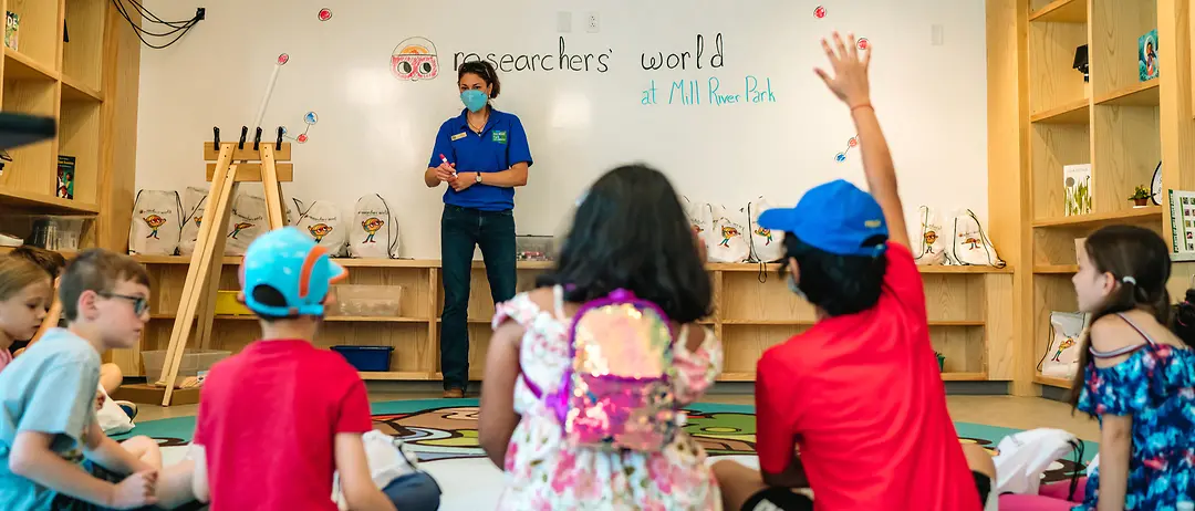 Henkel Researchers’ World instructor talking to children in a semi-circle sitting on the ground in a classroom.