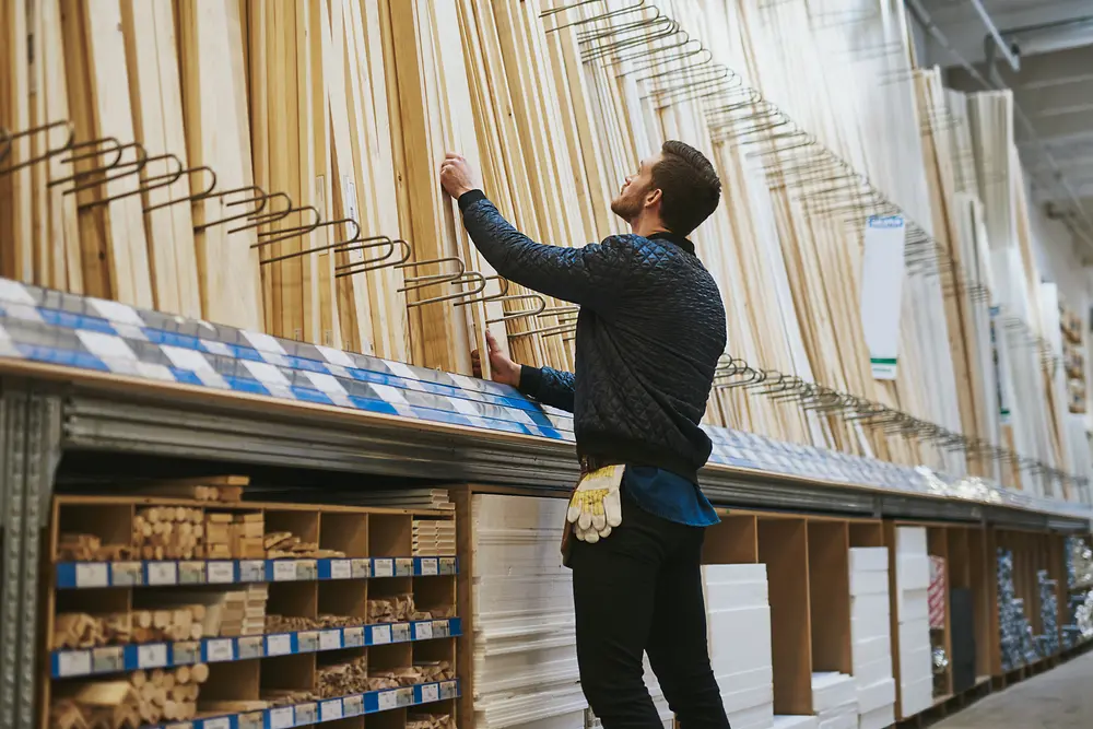 A man stands in front of a shelf of wooden slats in a building supply store.