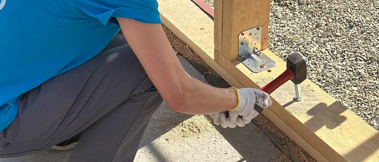 A Henkel employee hammers a nail into the wooden frame of the house.