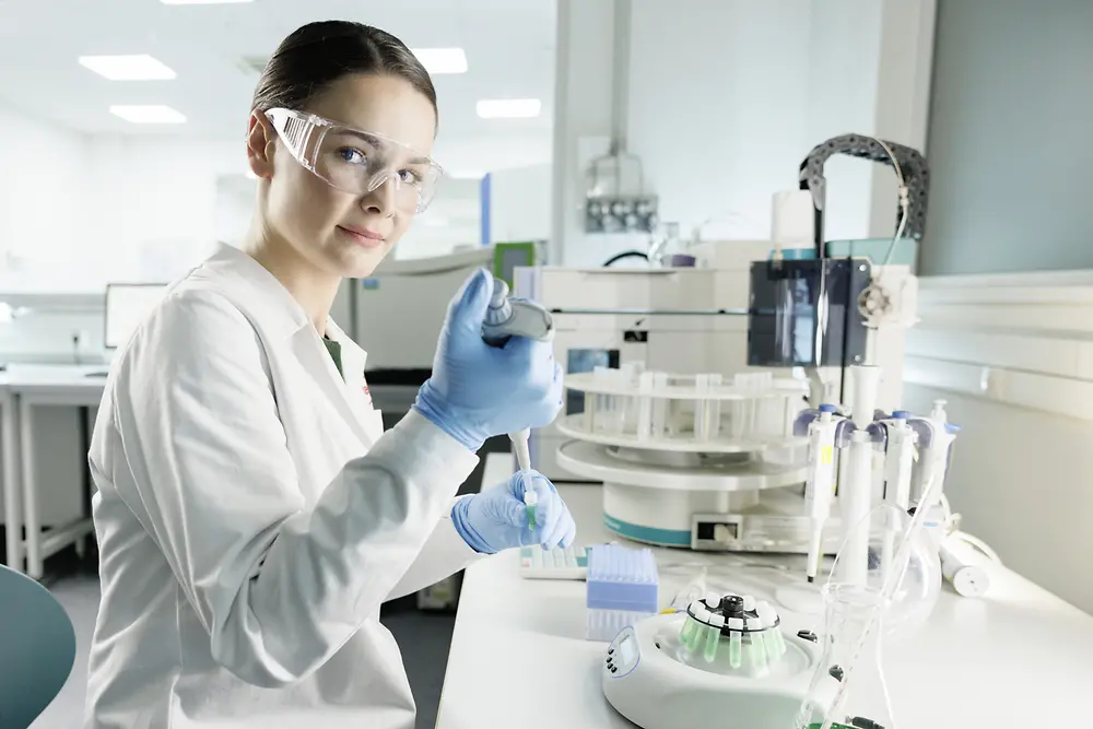 A female scientist is experimenting in a lab, wearing a lab coat and safety goggles.