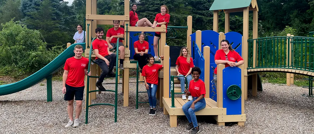 Henkel employees in red t-shirts pose in front of a playground.