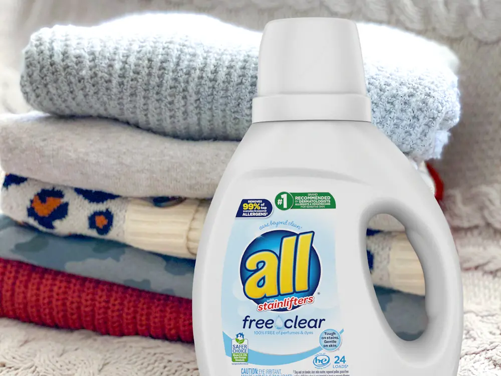 A bottle of all free clear sits in front of a stack of folded sweaters