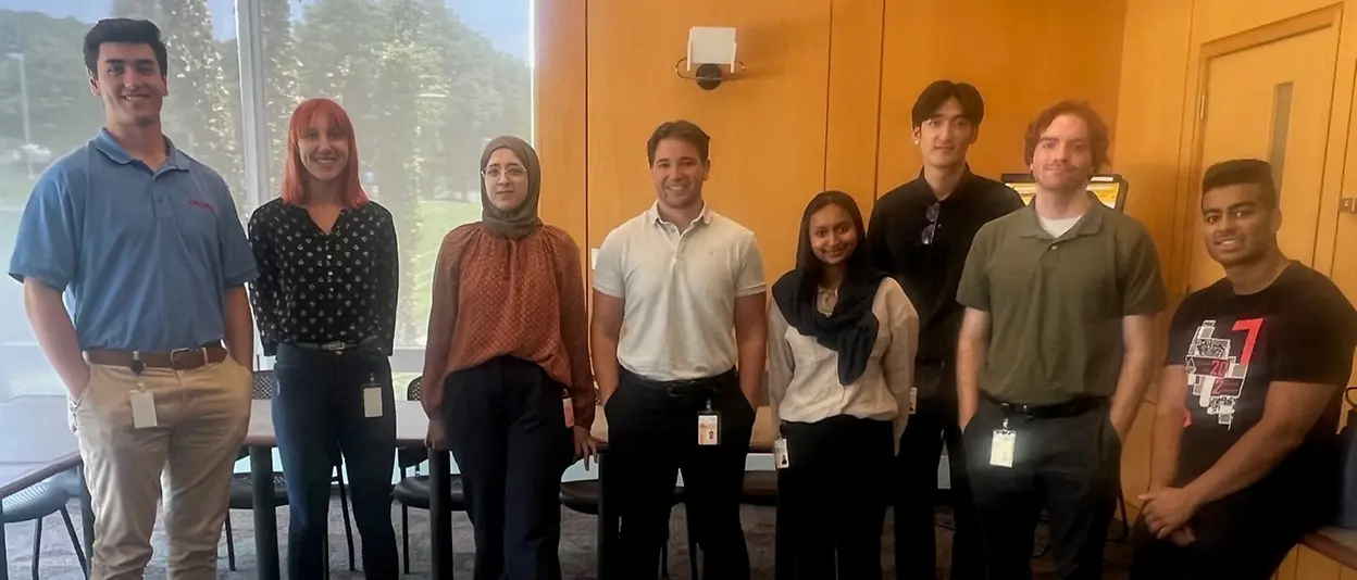 A small group of young people gather behind a cake decorated to celebrate National Intern Day