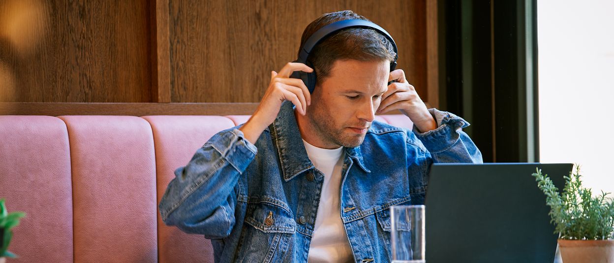 A man sits in front of his computer and puts on headphones.