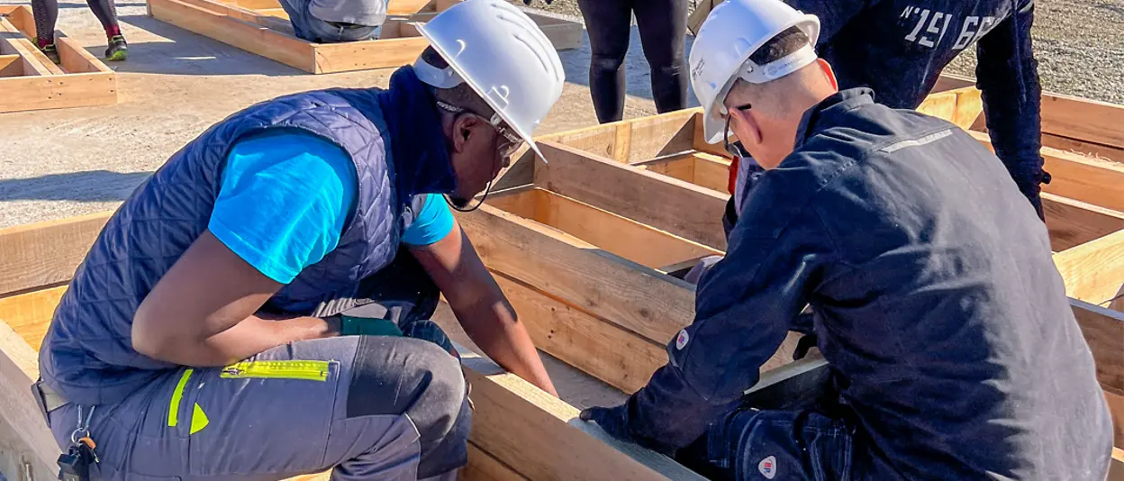 Two volunteers evaluate the wooden components for the house’s framework.