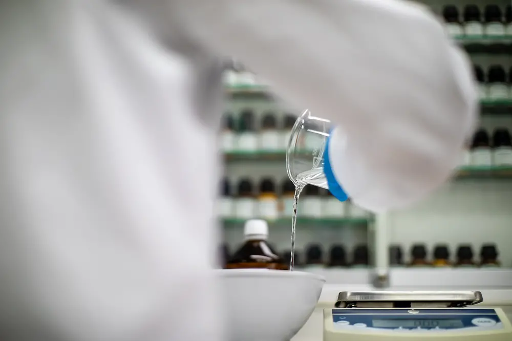 A person surrounded by amber glass bottles is pouring a liquid into a bowl.