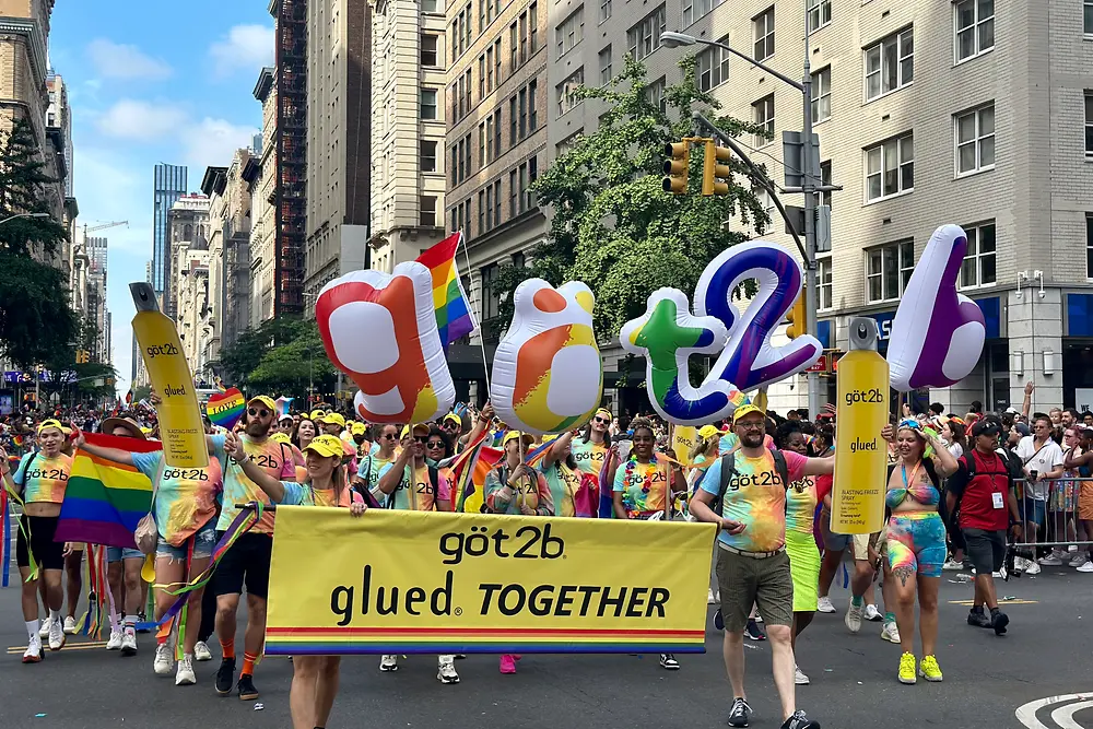 Large group of people in tie-dye tshirts marching through the streets of New York with rainbow letters spelling out got2b