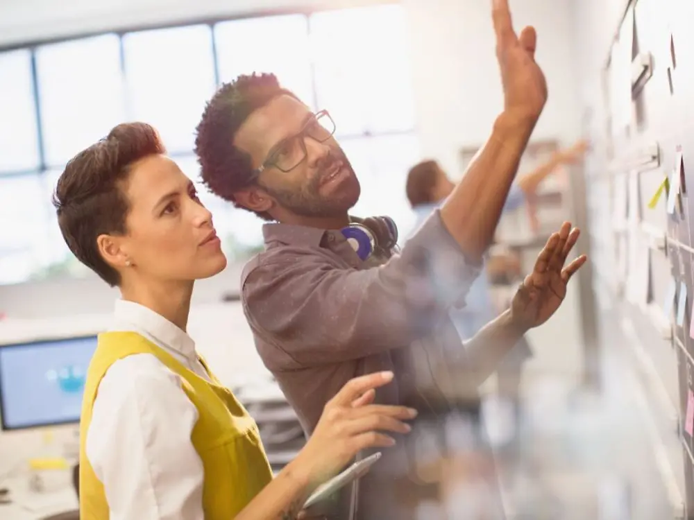 Male and female co-workers looking at a bulletin board.