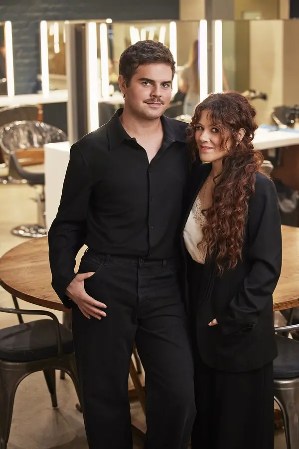 A man and a woman dressed in black in front of a mirror